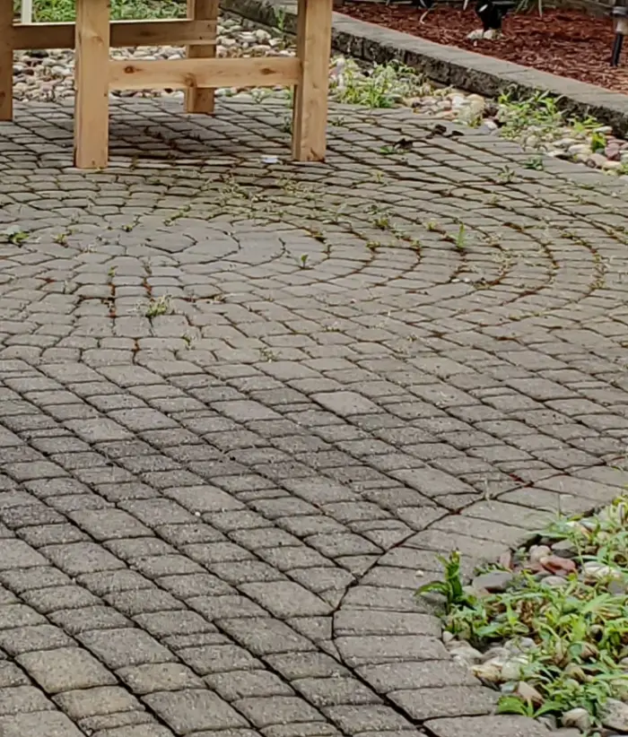 Weathered circular-pattern paver patio with weeds in the joints