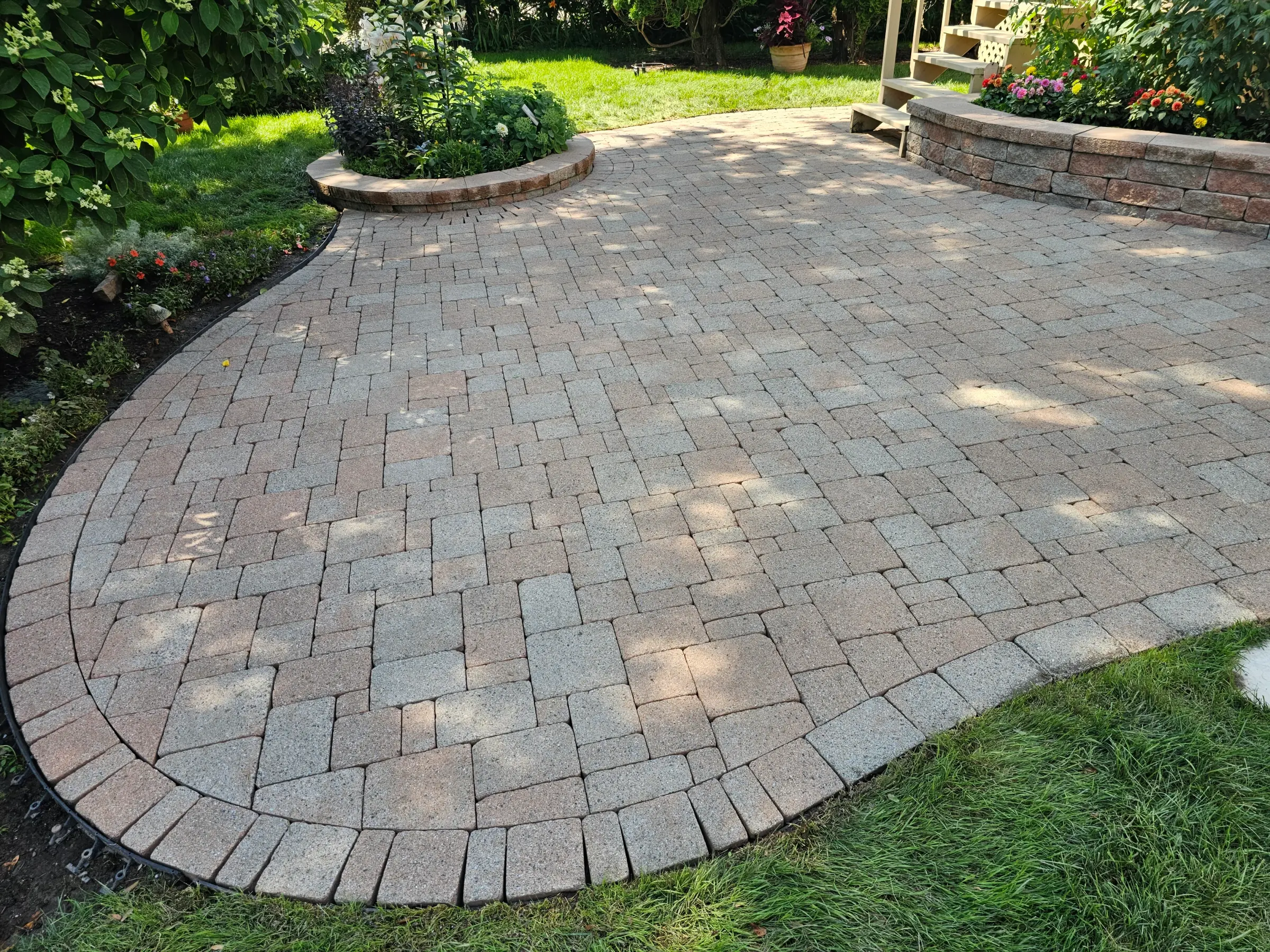 Restored multi-tone curved interlock patio framed by lush garden beds — a David's Lawns job