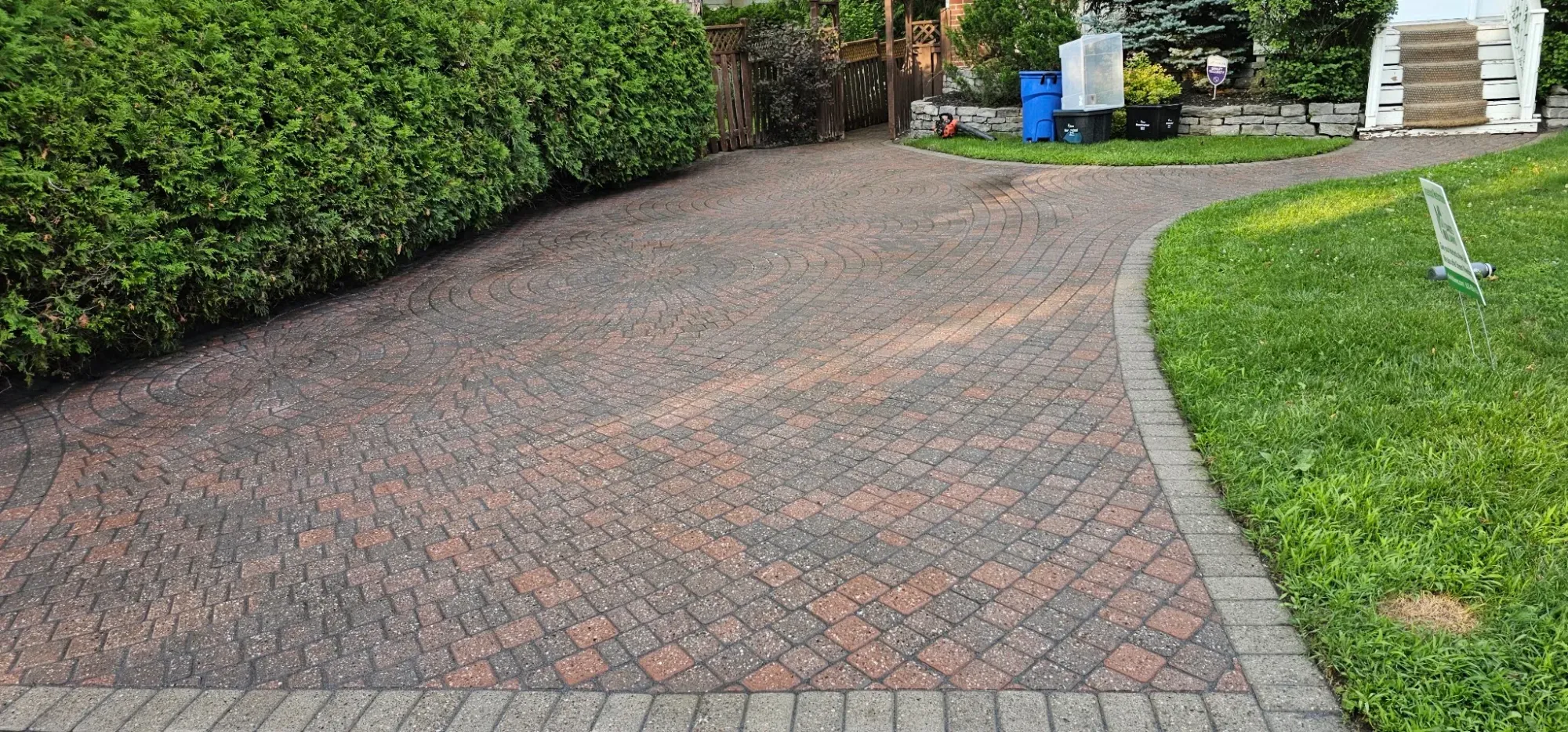 The same driveway freshly re-sanded, the joints sealed by new polymeric sand and the surface still wet — weed-free, crisp lawn edge